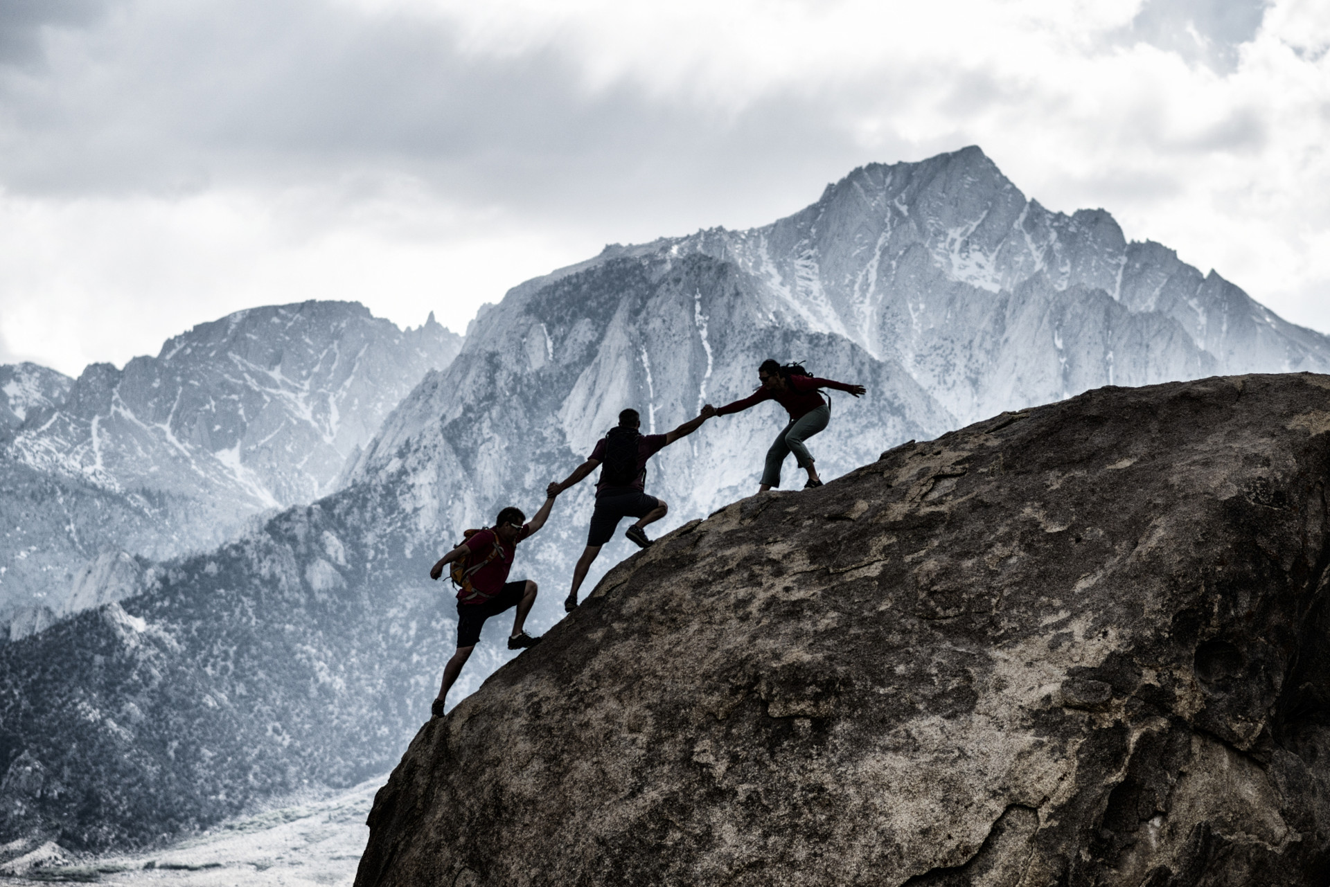 Three friends out rock climbing, helping each other in a dramatic setting